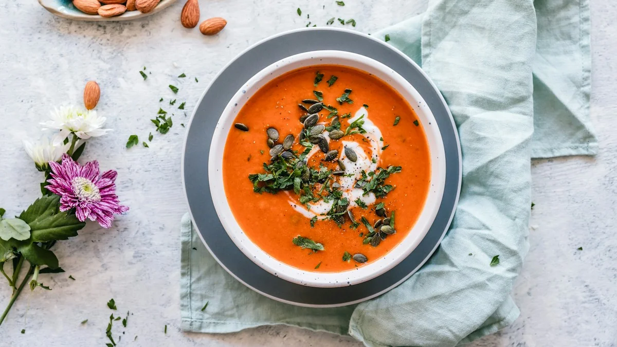 A steaming bowl of vibrant orange carrot and coriander soup garnished with a swirl of cream, freshly cracked black pepper, and fresh coriander leaves.