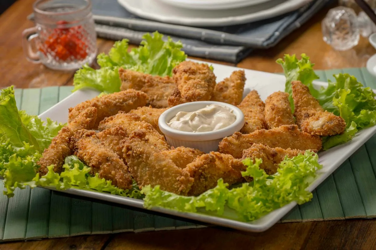 Golden crispy honey buffalo chicken tenders stacked on parchment paper, dripping with sweet spicy glaze with dipping sauce and parsley