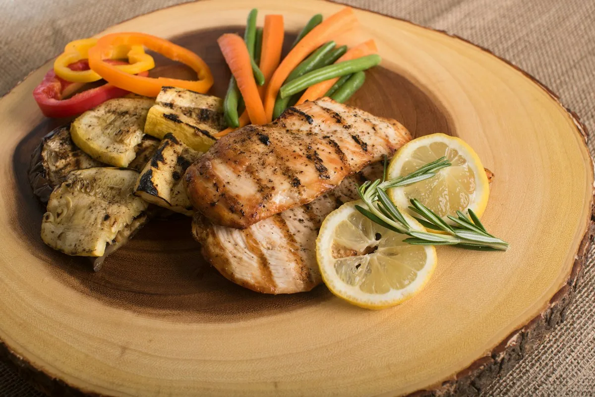 Golden crispy skin-on roasted chicken thighs in a skillet surrounded by tender roasted baby potatoes, fresh lemon wheels, and rosemary sprigs