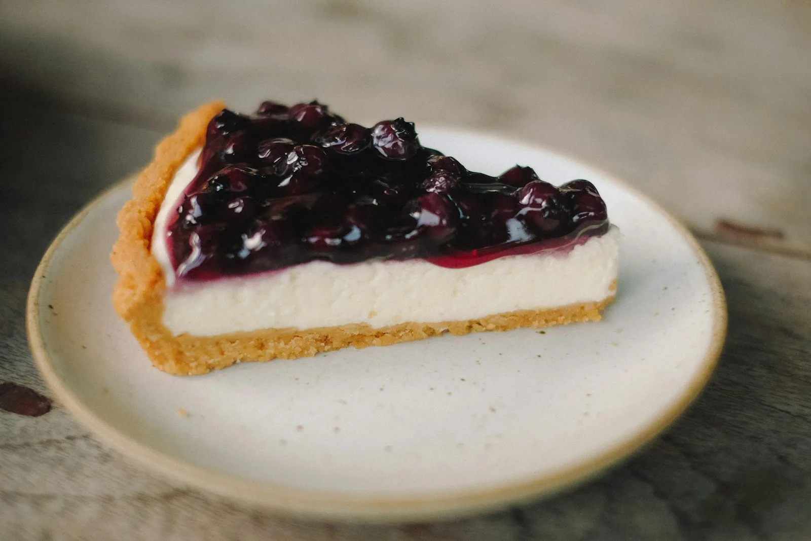 Slice of towering creamy New York cheesecake with golden graham cracker crust and fresh berry sauce