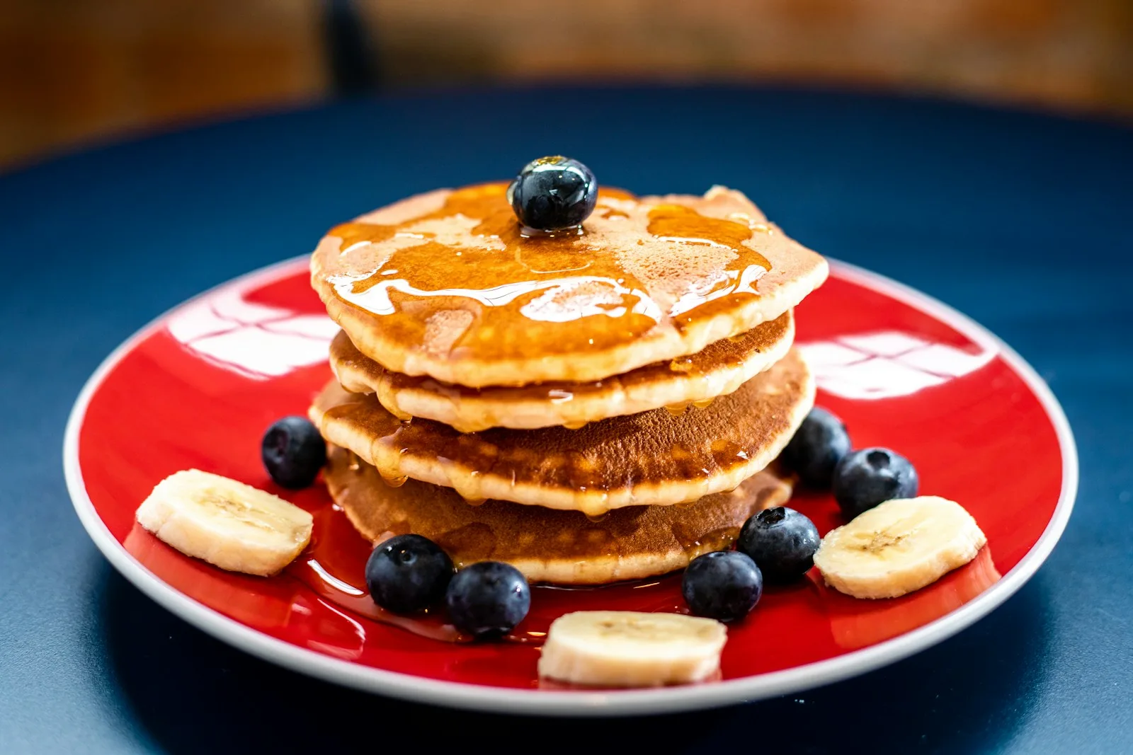 Towering stack of golden fluffy pancakes with melting butter and dripping maple syrup