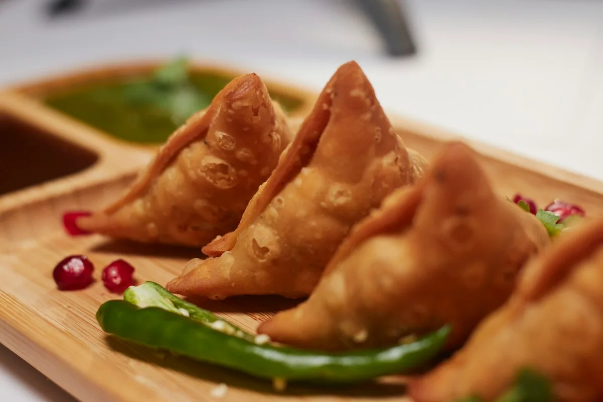 Platter of golden crisp mini triangular samosas garnished with fresh coriander leaves, lemon wedges, and a bowl of bright green mint chutney