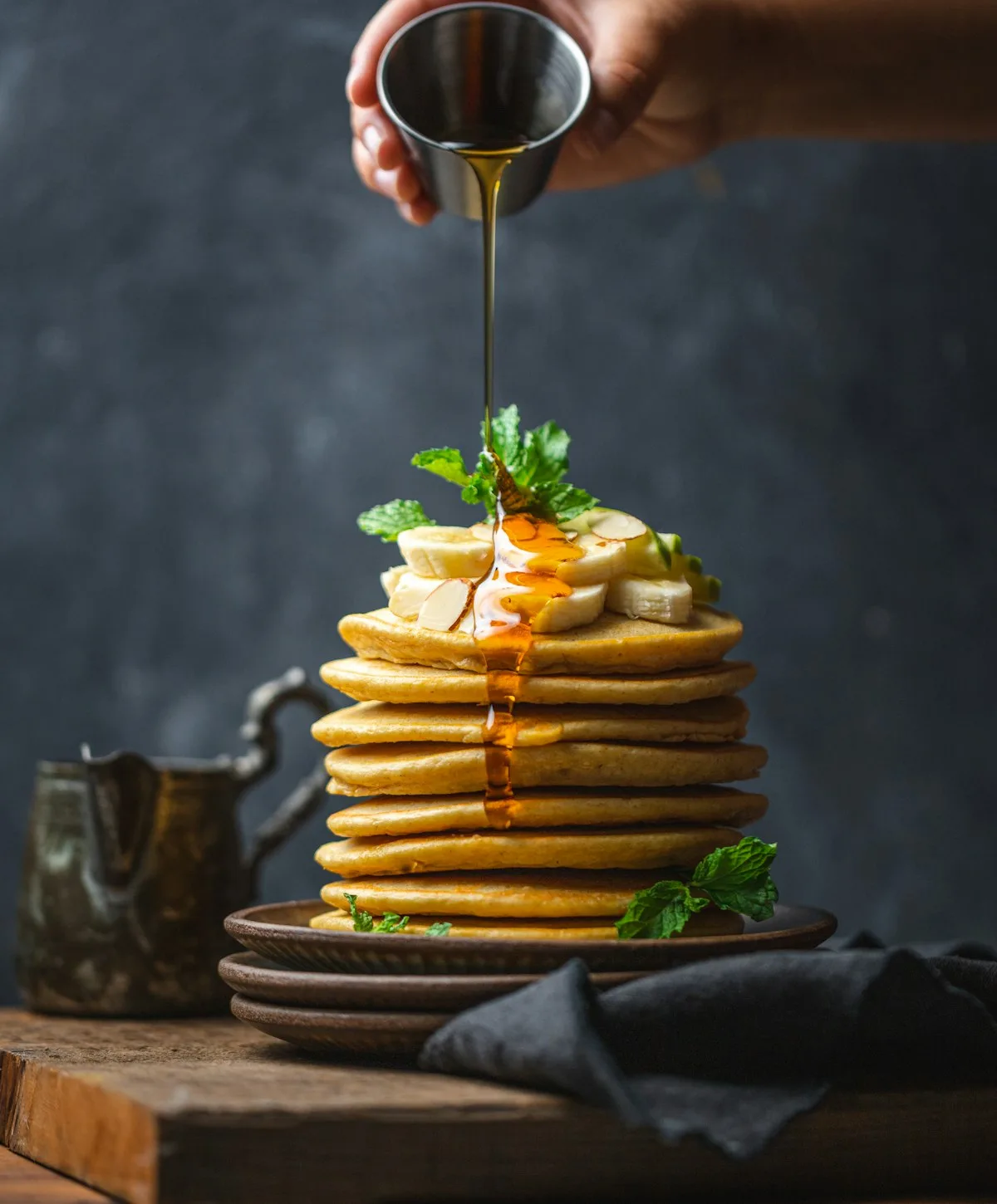 Tower of ultra-fluffy jiggly Japanese souffle pancakes topped with melting butter cube, powdered sugar dusting, and dripping maple syrup