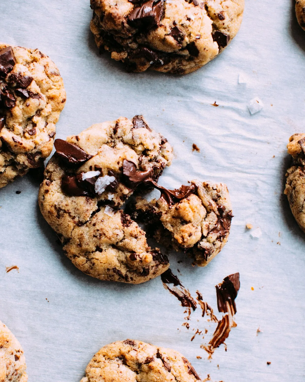 Giant thick chocolate chip cookie broken in half showing a rich molten gooey melted chocolate center on parchment paper