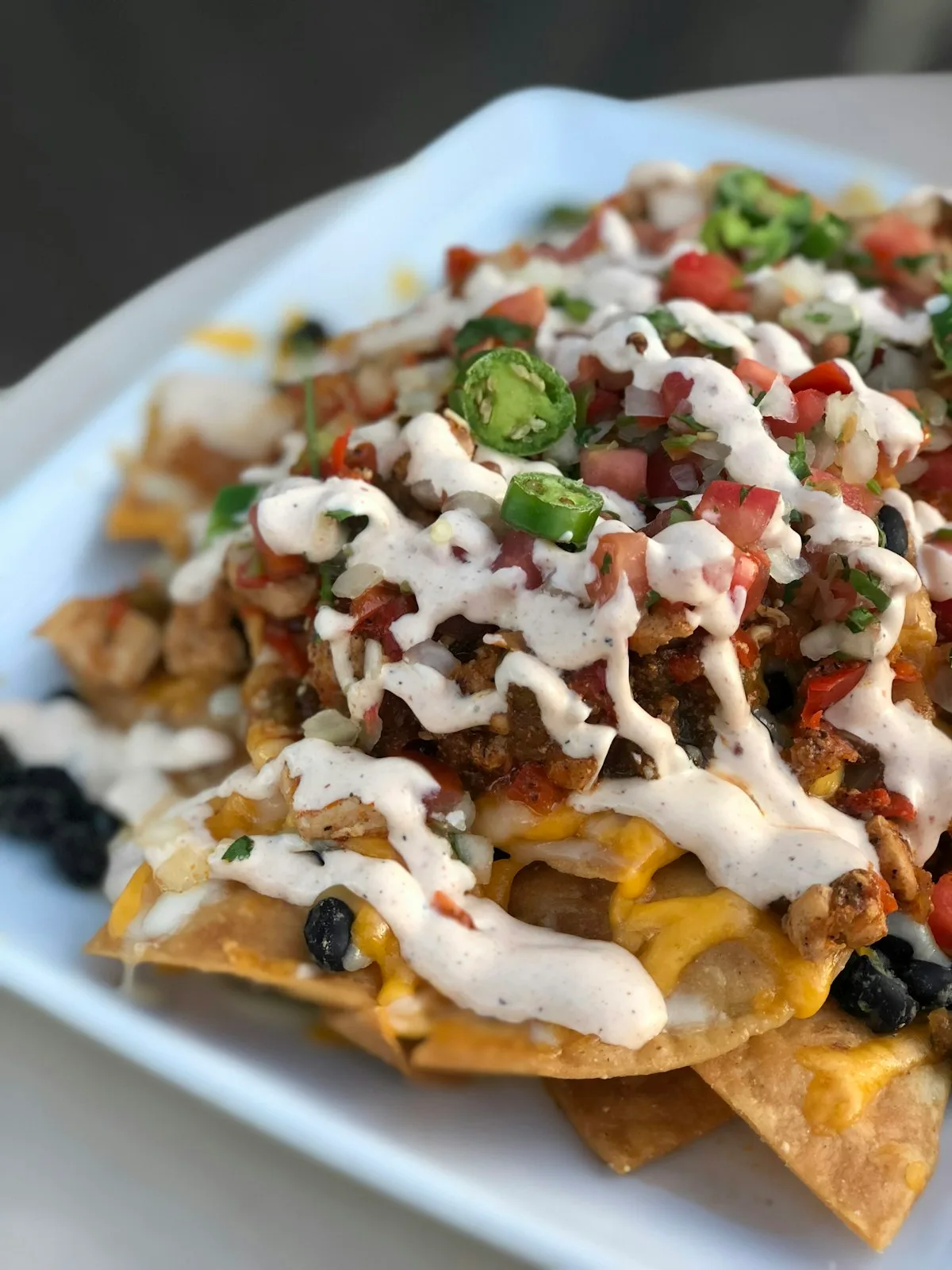Colorful platter of loaded sheet pan nachos smothered in melted cheese, seasoned ground beef, jalapeños, black beans, and dollops of fresh guacamole