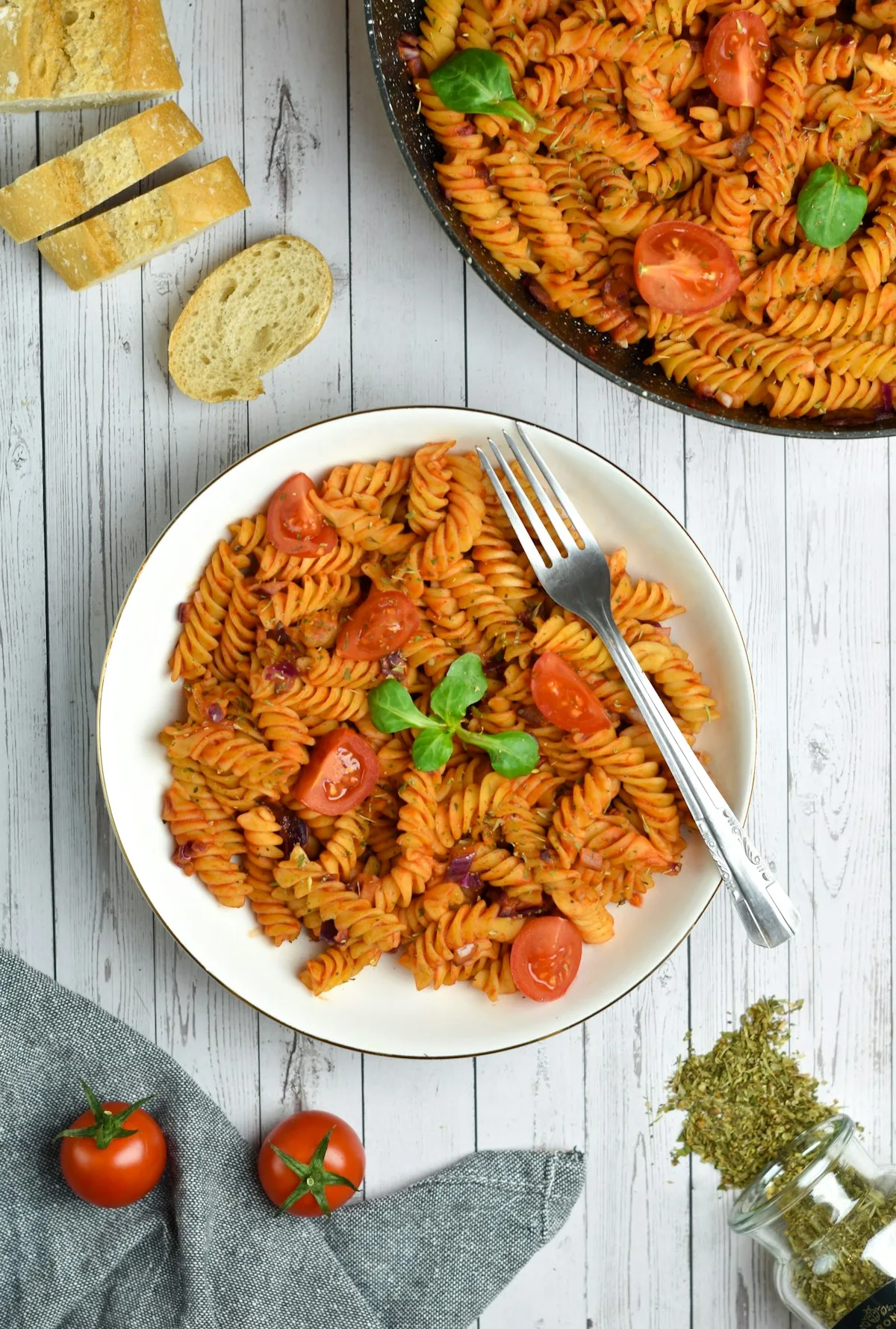 Baking dish of creamy baked feta pasta with blistered red cherry tomatoes, fresh basil leaves, and rigatoni noodles